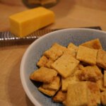 Sauerteig-Cheddar-Cracker auf Holzbrett – knuspriger Snack aus Sauerteigstarter; Sauerteig-Cheddar-Cracker selbst gemacht – goldbraun gebacken; Resteverwertung mit Sauerteigstarter – knusprige Cheddar-Cracker
