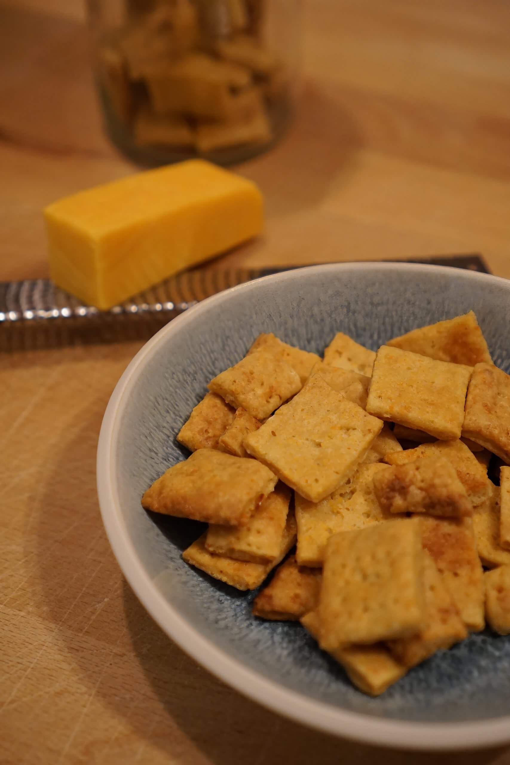 Sauerteig-Cheddar-Cracker auf Holzbrett – knuspriger Snack aus Sauerteigstarter; Sauerteig-Cheddar-Cracker selbst gemacht – goldbraun gebacken; Resteverwertung mit Sauerteigstarter – knusprige Cheddar-Cracker